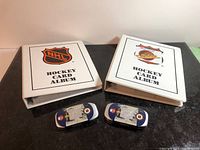 Two white hockey card albums and two small collectible tins on black surface.