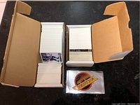 Two open boxes of hockey cards on a black surface, cards packed and standing vertically, one shows visible player images including goalies and skaters.