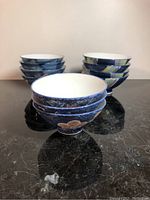 Six blue Japanese style ceramic bowls with floral exterior patterns on dark blue background, white interiors, arranged in stacks.