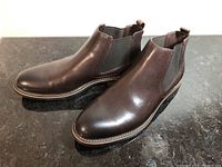 Pair of brown leather slip-on boots shown on black marble surface. Side elastic panels and pull tabs visible.