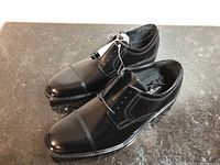 Pair of black leather dress shoes showing side and top, polished toe cap with detailed stitching.