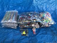 Overview photo showing multiple sealed packages of party novelty items including straws, glasses, noses, and sticky wall throwers on a blue tarp.