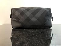 Front view showing the rectangular toiletry bag with black checkered pattern and leather bottom accents.