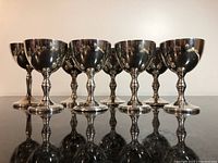 Front view of eight silver plated goblets standing on a reflective black surface showing their shape and uniformity.