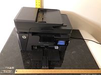 Front angled view of HP LaserJet Pro MFP printer showing paper trays and power button lit.