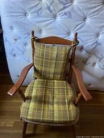 Front view of antique wooden kids chair with plaid cushioned seat and backrest, showing spindle back and wooden armrests.