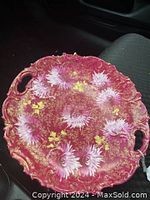 Photo showing the vintage serving plate with scalloped edges, pinkish-red base, white floral designs, gold detailing, and two handles.