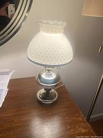 Glass shaded electric table lamp illuminated on wooden surface showing hobnail texture and metal base.