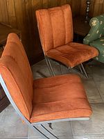 Two orange fabric chairs with chrome sled bases positioned side by side in front of wood paneled wall