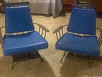 Front view of both chairs showing blue vinyl cushions, iron frames, and wooden armrests