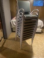 Stacked view of 10 metal-frame outdoor chairs with green seating fabric, showing the profile and armrests