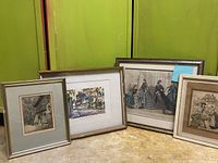 Four framed prints leaning against green wall showing variety in size and style including a fashion print with figures and architectural prints