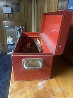 Red metal tool box with open lid, showing exterior condition and handles, some rust visible on metal