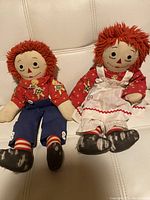 Front view of the two raggedy dolls seated showing full body details including clothing, yarn hair, and painted facial features.
