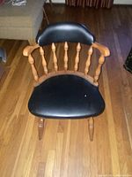 Wooden chair with spindled backrest and black upholstered padded seat and backrest on a hardwood floor.