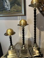 Full view of the three candle holders with gold spherical candles placed on top, showing their varying heights and twisted wood stems with metallic bases and tops.