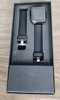Smart watch and additional wristband in original box with black foam padding.