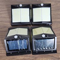 Four black solar powered LED wall lights featuring solar panels on the front, multiple LEDs on the top surface, PIR motion sensors, and CDS night sensors.
