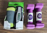 Photo showing one pack of Gaiam 4 lb walking weights in green, grey and black with fabric and mesh covering alongside a pair of purple neoprene 3 lb hand weights.