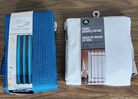 Photo of two new fabric shower curtains side by side, one blue by HomeTrends and one white by Mainstays, both packaged.