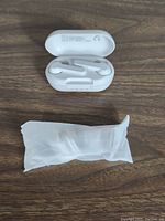 Open charging case containing a pair of white MPOW Mbits S earbuds alongside a sealed white bag with additional ear tips.