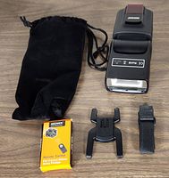 Neewer TT560 electronic flash speedlite with black pouch, remote control box, flash stand, and strap displayed on a wooden surface.