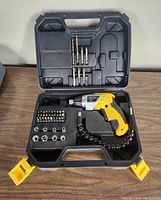 Opened hard plastic case containing yellow and black cordless screwdriver, multiple bits, socket heads, and flexible extension shaft, all organized in molded inserts.