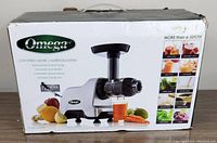 Photo of the Omega CNC80S Low Speed Juicer in its original retail box featuring images of fruits, vegetables and glass of fresh juice, highlighting its nutrition system, low speed 80 RPM motor, and compact design.