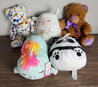 Five plush toys including three Squishmallows and two bears. Unicorn, llama, panda Squishmallows with scents and two traditional plush bears: one brown and one multi-colored.