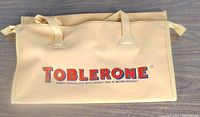 Front view of beige/yellow duffle bag with Toblerone logo and text.