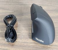 Black ergonomic vertical wireless mouse and USB charging cable side by side on a wooden surface.