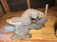 RAE bench vise with extensive surface rust and signs of wear, blue paint mostly worn through but complete with mounting base and screw handle.