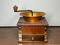 Front view of vintage hand crank coffee grinder with brass bowl and wooden base