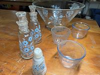 Photo showing two Culver glass decanters with blue flowers and stoppers, large matching bowl, three smaller clear glass cups, and a small salt shaker with blue flower design.