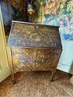 Photo of entire drop front desk closed, showing decorative metal hardware on drop front panel and natural wood grain.