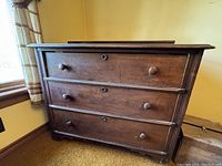 Front view showing three full-width drawers with wooden knobs and lock keyholes.