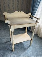 Front angled view of the early washstand showing the white and gold paint, turned towel bars, lower shelf, and carved back panel.