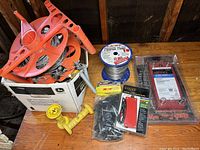 Overall lot display showing orange plastic electric fence posts, spool of wire, clips in bag, and fence controller in packaging.