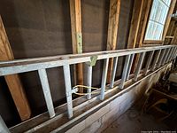 Long aluminum extendable ladder leaning against wall with visible rungs and extension ropes.