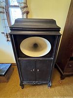 Front view of black wooden Brunswick floor phonograph cabinet with large speaker horn opening and double-door front panel.