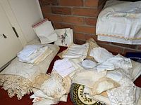 Wide view of linens piled together on surface showing doilies, embroidered serviettes and lace tablecloth edges.