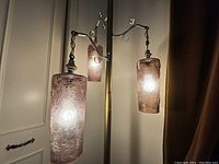 Close-up of two of the hanging cylindrical glass lampshades with etched floral design and warm light visible inside.