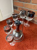 Front angle showing the wine decanter in the metal stand with six glasses arranged around it