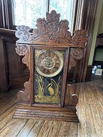 Front view of the wooden Sessions gingerbread clock showing intricate carved designs and gold heron illustration on glass.