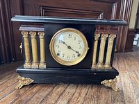 Front side view of the black mantel clock with gold and faux marble columns and ornate feet.