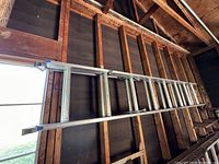 Side view of aluminum extension ladder hanging horizontally on a wooden wall structure, showing rungs, railings and blue end caps.