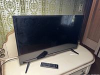 Front view of the Toshiba 32-inch LED television with remote placed in front of it on a cream-colored table.