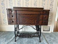 Front view of wooden sewing cabinet showing multiple drawers and cast iron treadle base.