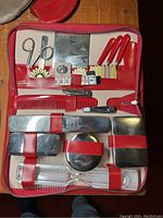 Open red travel kit showing silver-tone containers secured by red elastic bands, grooming scissors, nail clippers, toothbrush, comb, four red-handled small tools, and two small pouches