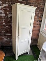 Front view of the tall white wooden wardrobe showing its single door with three recessed panels and metal knob.